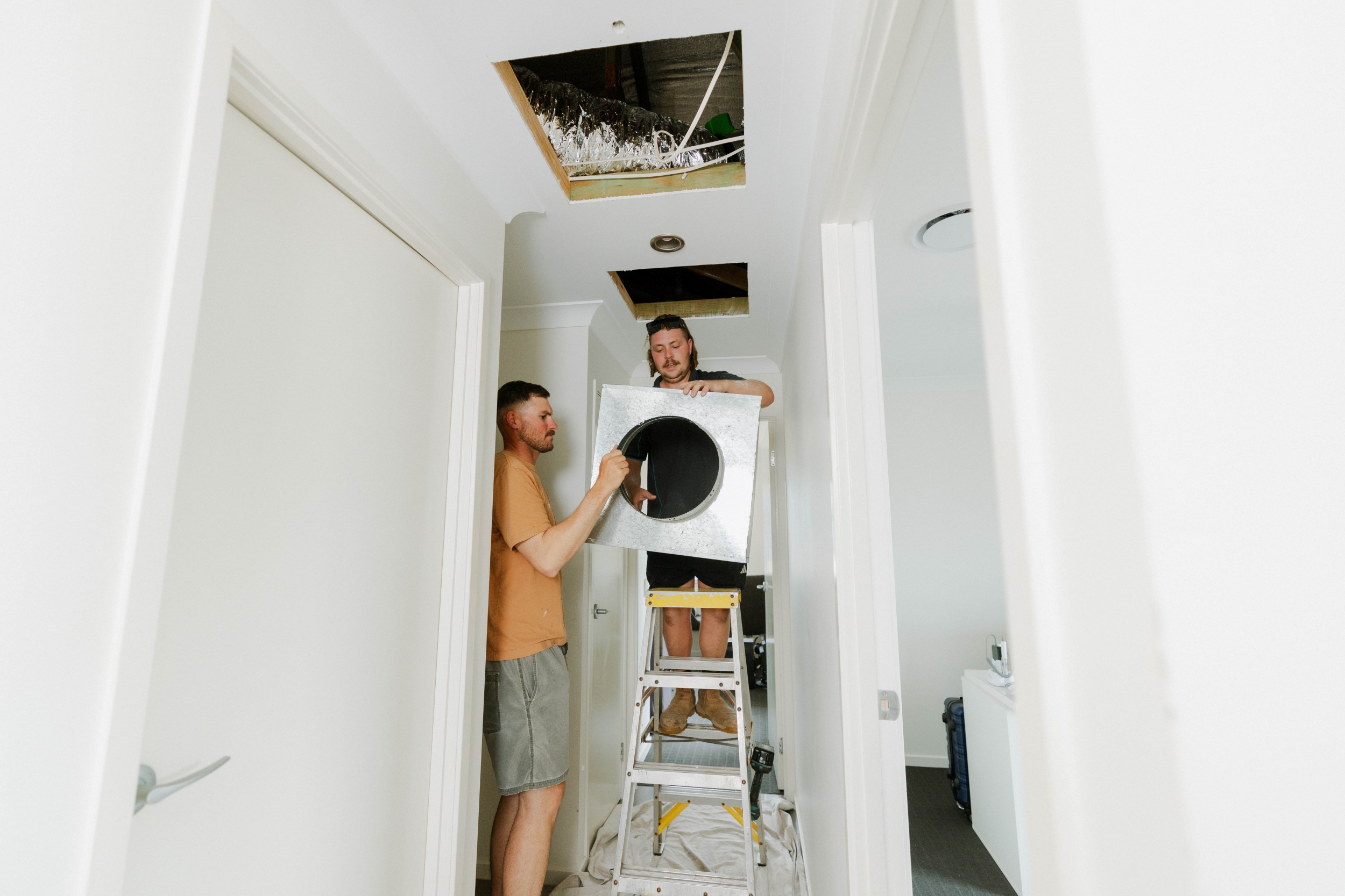 Parker Air Solutions team lifting ducted unit into ceiling space in Kallangur home