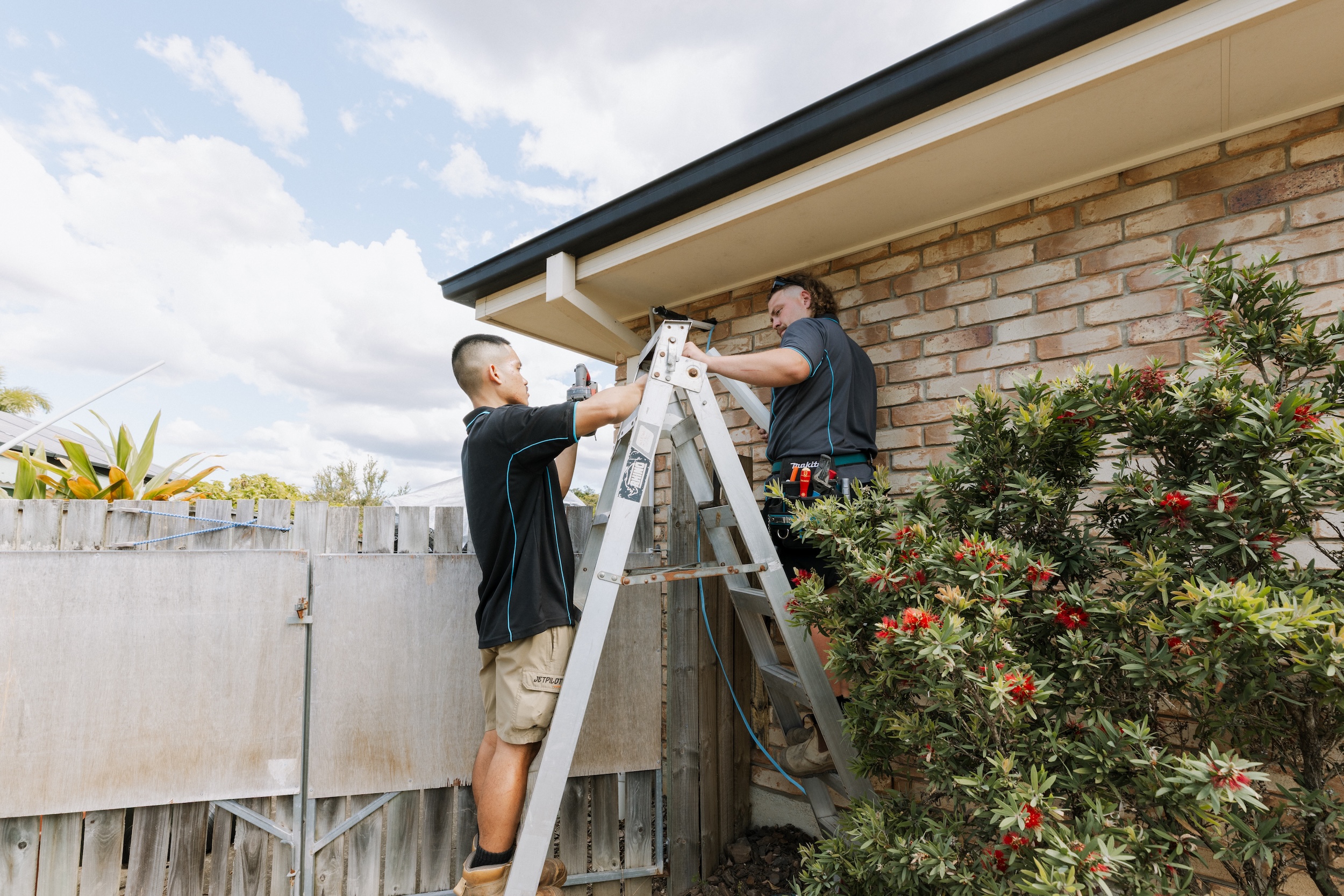 Two aircon technicians installing outdoor pipes safely